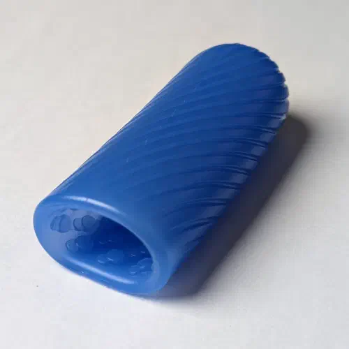 A blue Arcwave Ghost silicone stroker lying on a white surface, showing its spiral-ribbed outside and the bumpy texture inside the opening.